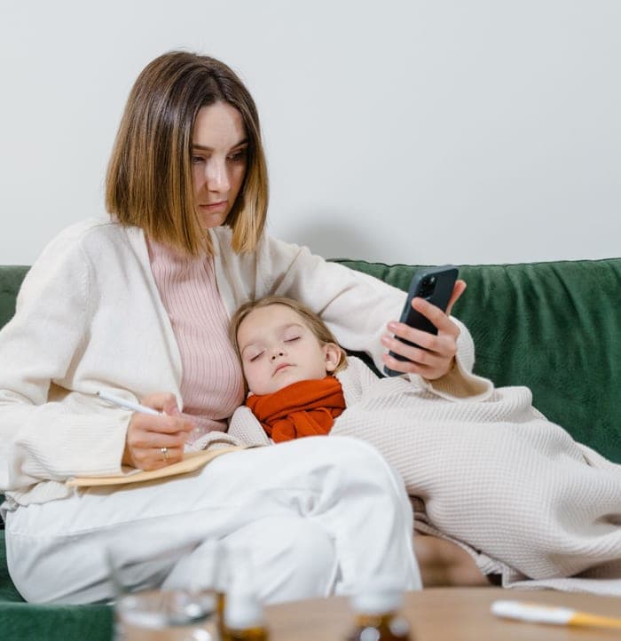 Parent looking up a doctor on her phone while caring for a sick child